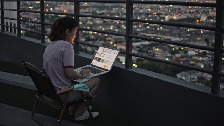How To Move Up The Ladder In Your Remote Job - Dolly shot of businesswoman in casual clothes working on laptop in roof terrace at night,Slow motion